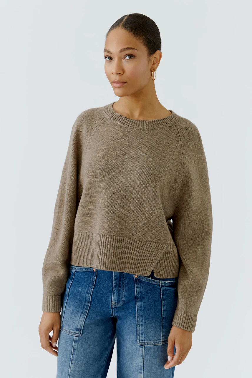 Damen-Pullover: Frau im beigen Pullover mit Raglanärmeln und blauer Jeans, schlicht und modern.