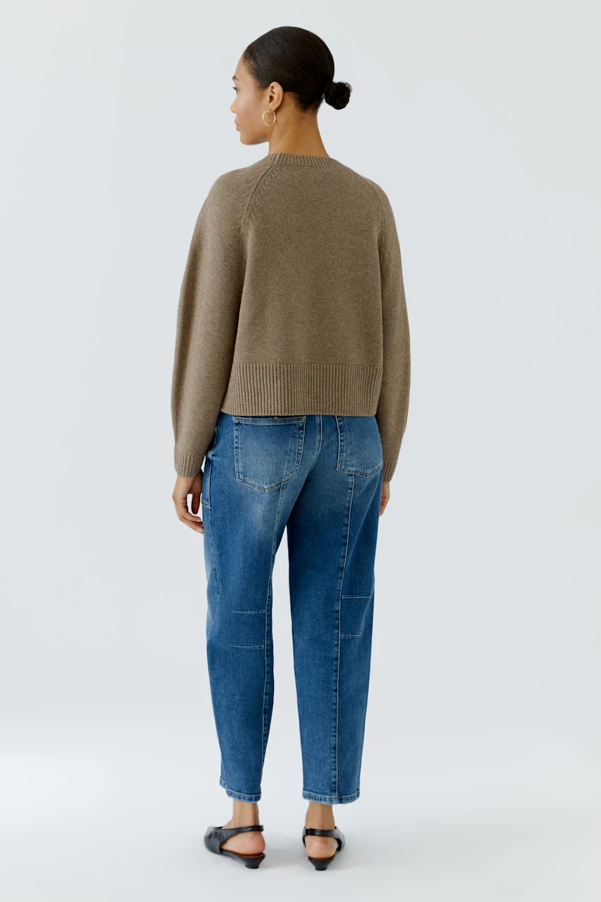 Frau im beigen Pullover und blauer Jeans, von hinten gesehen. Lässiger Look für den Alltag.