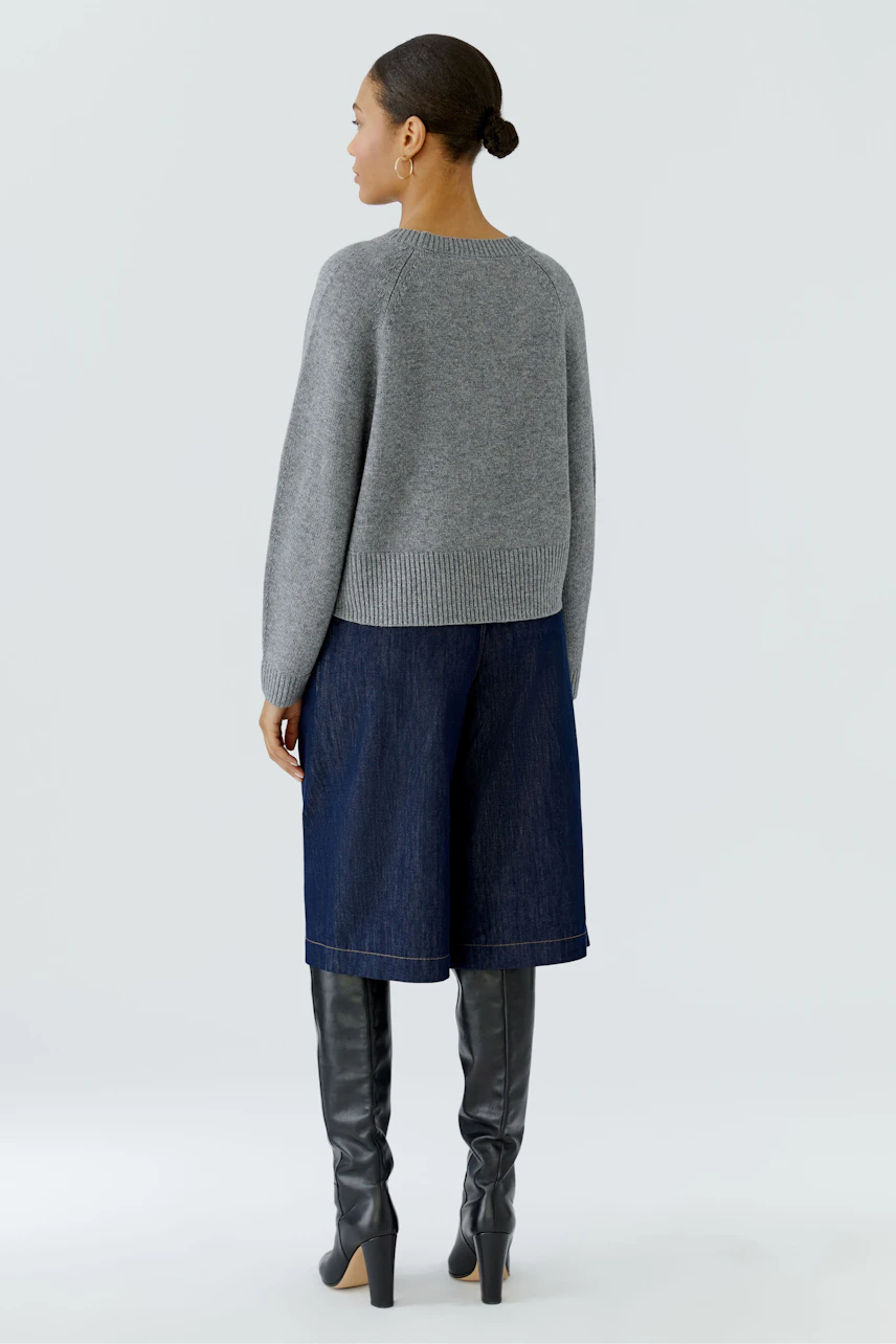 Casual women's pullover: Woman in a grey pullover, denim culottes, and knee-high boots, viewed from the back.