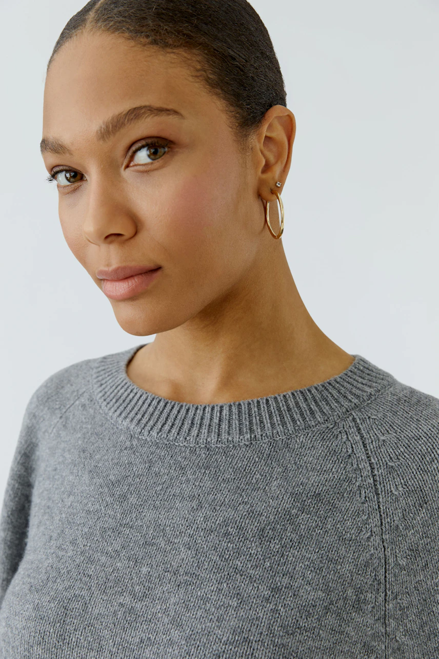Woman in a grey pullover with a simple design, looking confidently at the camera.