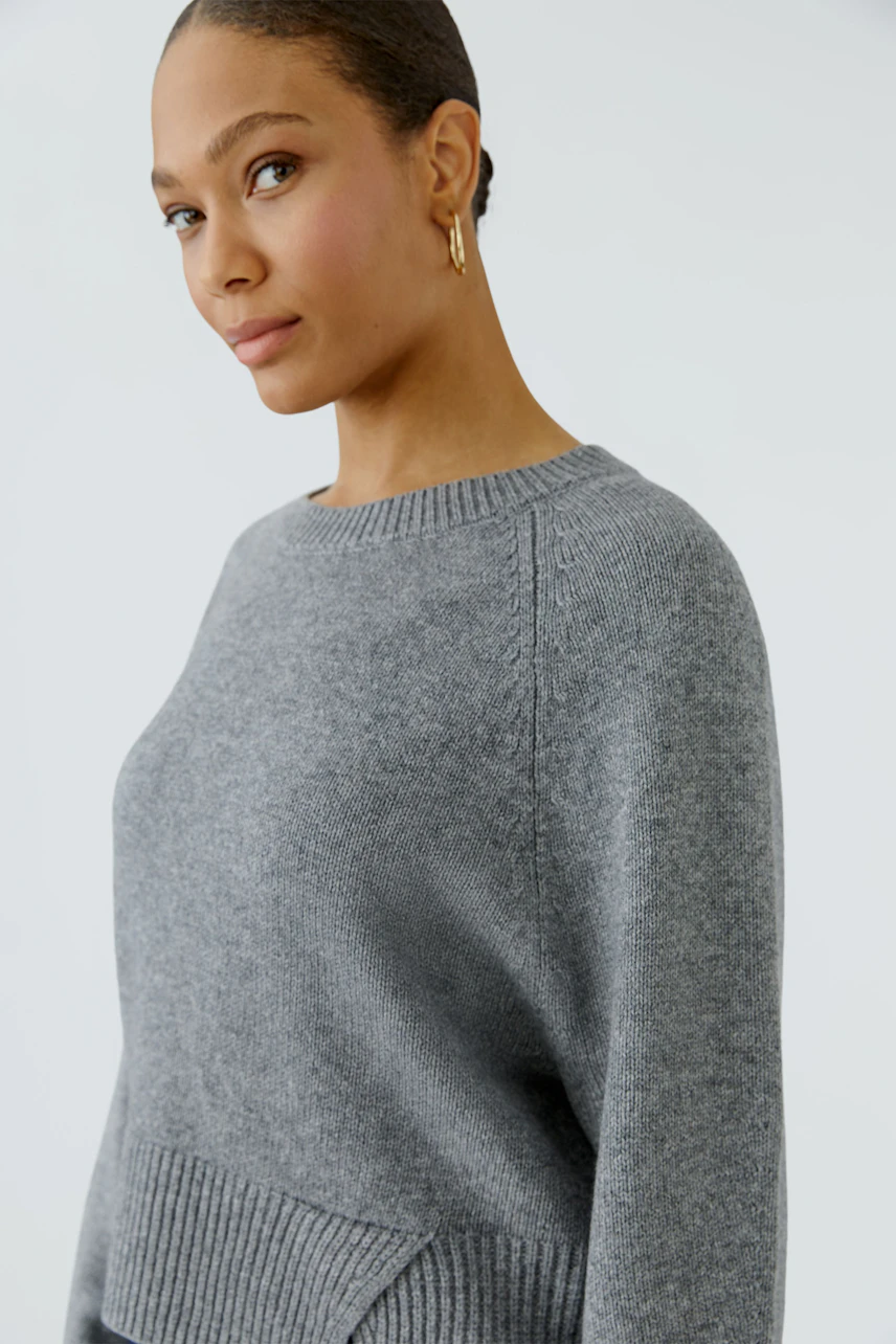 Casual women's pullover: Woman in a grey knit pullover with ribbed cuffs and a relaxed fit.