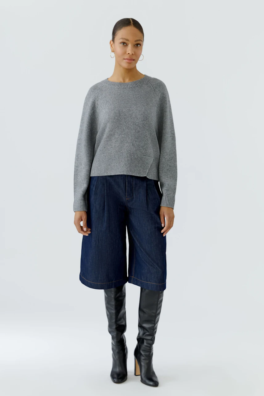 Casual women's pullover: Woman in a gray pullover with denim culottes and knee-high black boots.