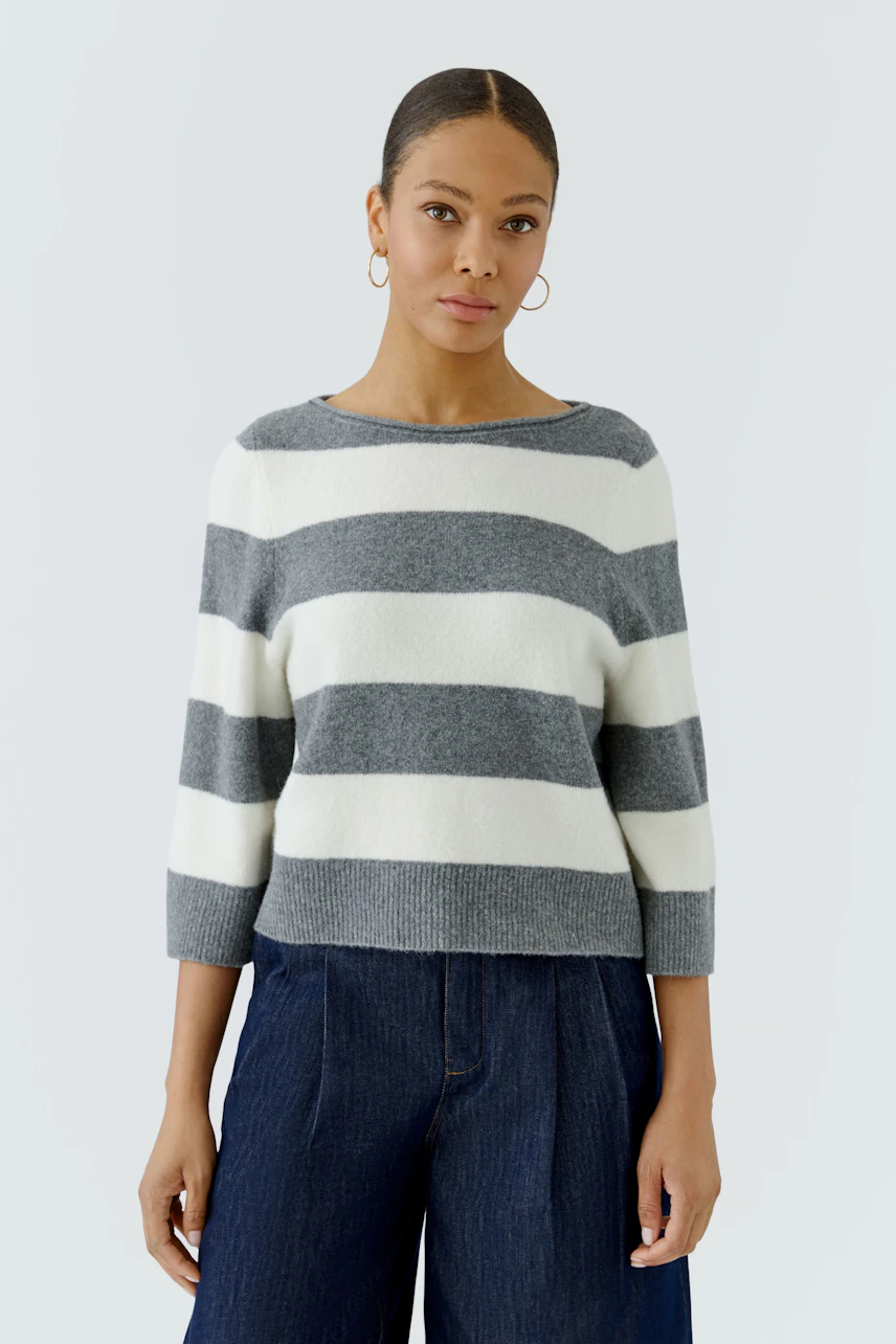 Casual women's pullover: Woman in a striped grey and white pullover with wide-leg jeans, looking poised.