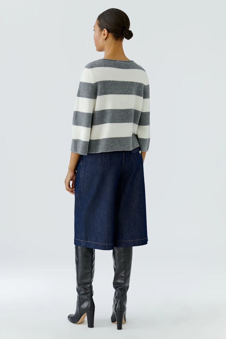 Casual women's pullover: Woman in striped pullover, denim culottes, and knee-high boots, facing away.