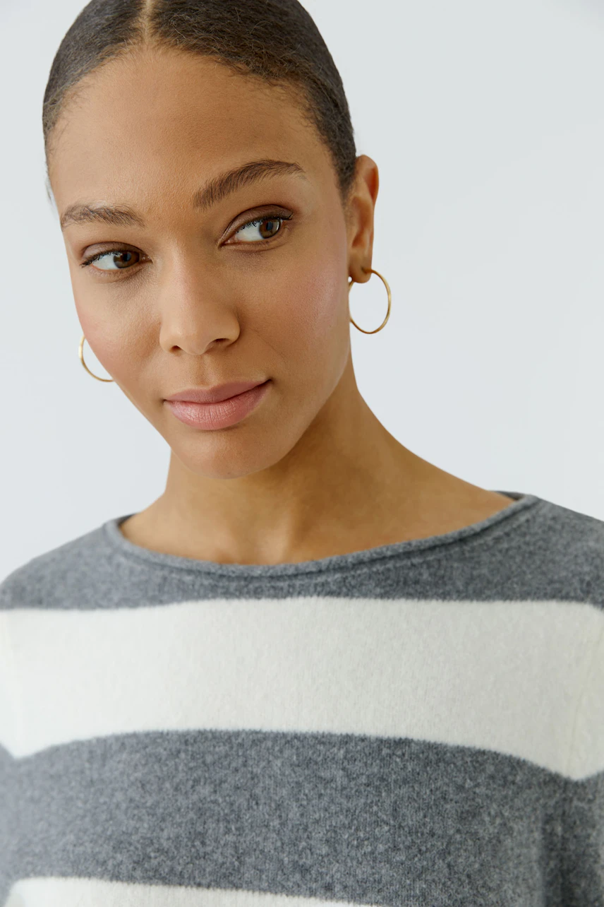 Casual women's pullover: Woman in a grey and white striped pullover with gold hoop earrings.