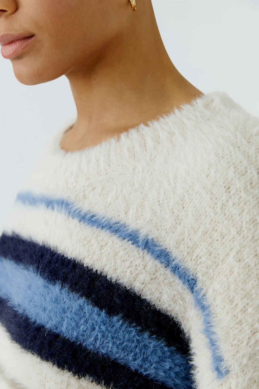Flauschiger Damen-Pullover: Frau im cremefarbenen Pullover mit blauen Streifen, Nahaufnahme des Designs.