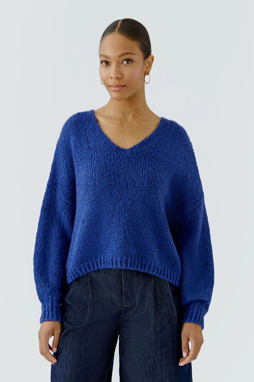 Casual women's pullover: Woman in a blue knit pullover with relaxed fit and dark jeans, exuding confidence.