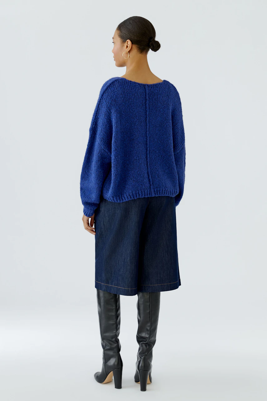 Casual women's pullover: Woman in a blue knit pullover with wide-leg jeans and knee-high boots, looking sideways.