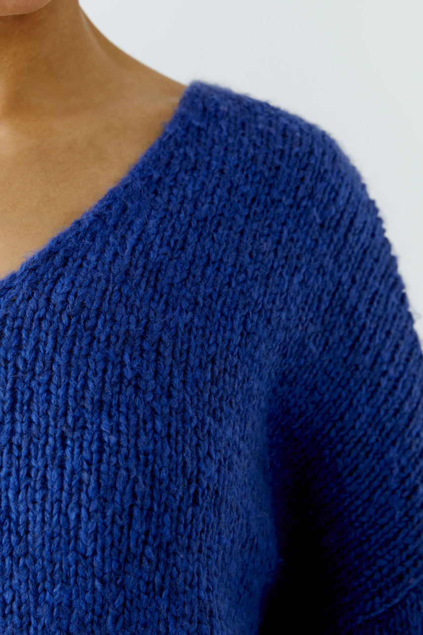 Cozy blue pullover: Woman in a textured knit pullover with a deep V-neck, showcasing casual comfort.