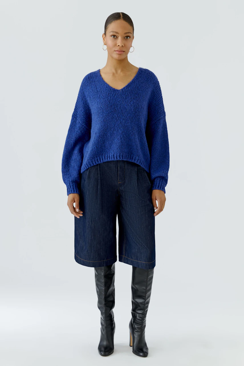 Casual women's pullover: Woman in blue knit pullover, denim culottes, and black knee-high boots.