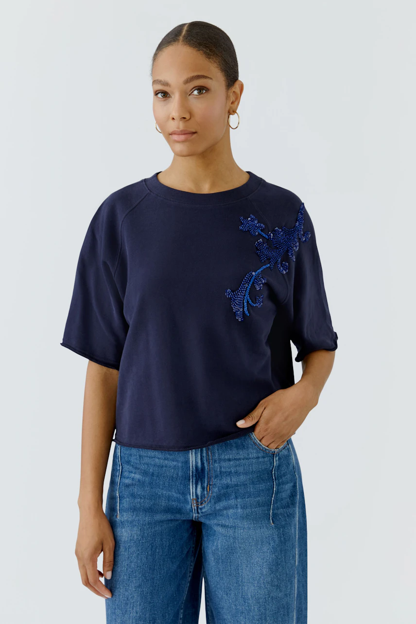 Casual women's sweatshirt: Woman in navy sweatshirt with floral detail, paired with blue jeans, looks relaxed.