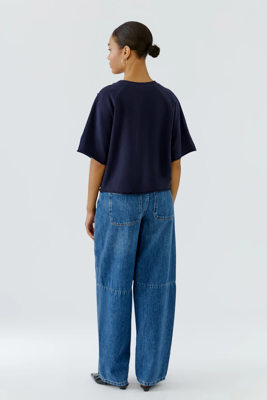 Casual sweatshirt: Woman in navy sweatshirt and wide-leg jeans, viewed from the back.