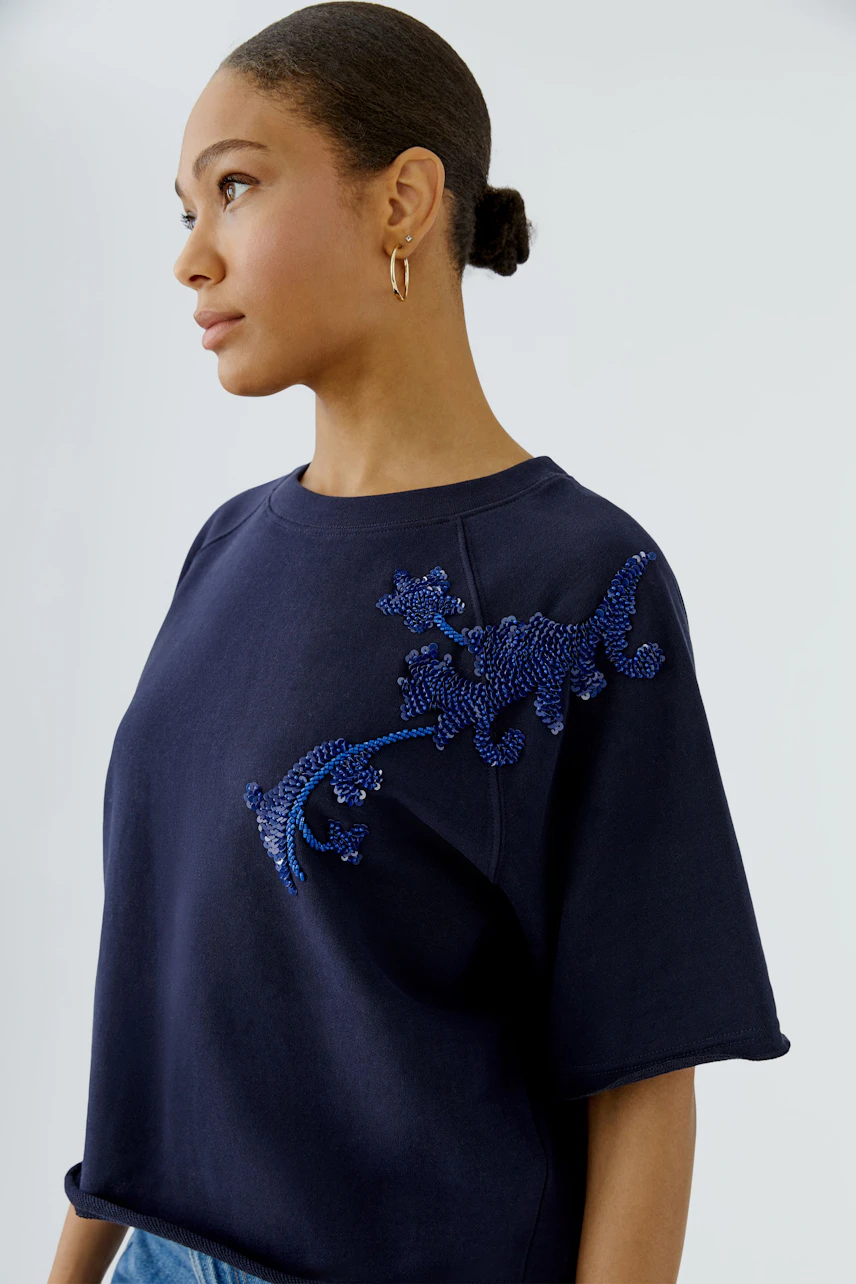 Woman in navy sweatshirt with blue beaded design on shoulder, short sleeves, and casual fit.