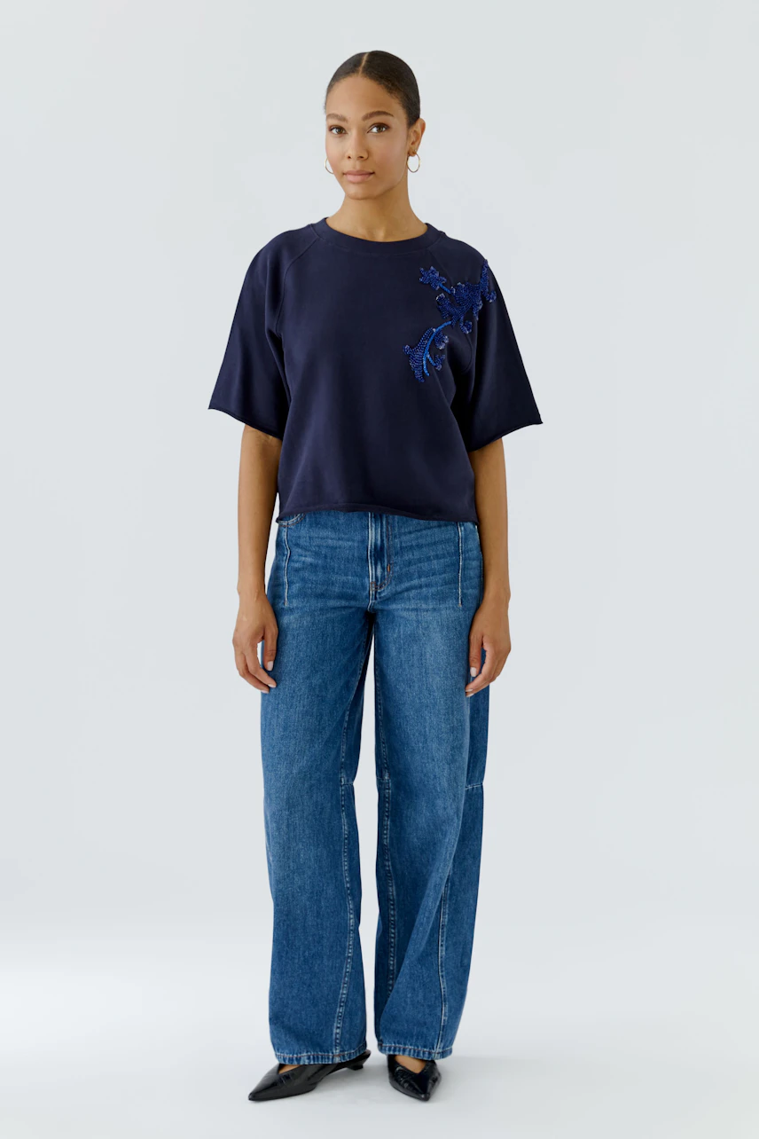 Casual women's sweatshirt: Woman in navy sweatshirt with floral embroidery, paired with wide-leg jeans.