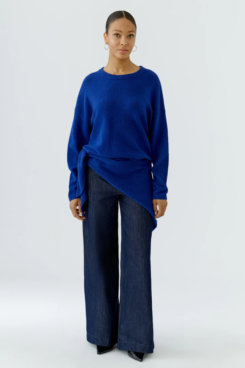 Frau trägt blauen Pullover und weite Jeans. Schal nicht sichtbar.