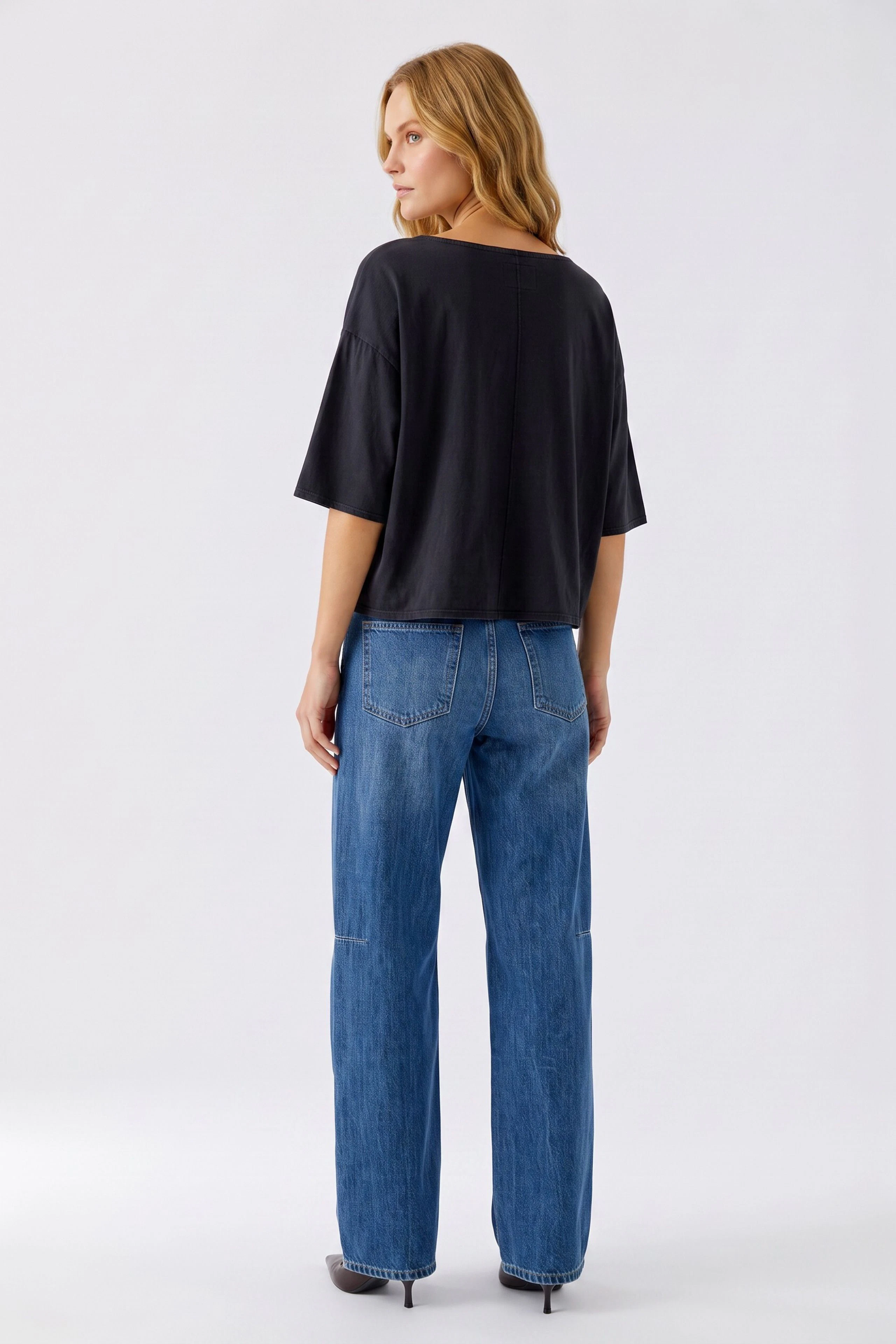 Casual women's T-shirt: Woman in a loose black T-shirt and blue jeans, standing confidently.