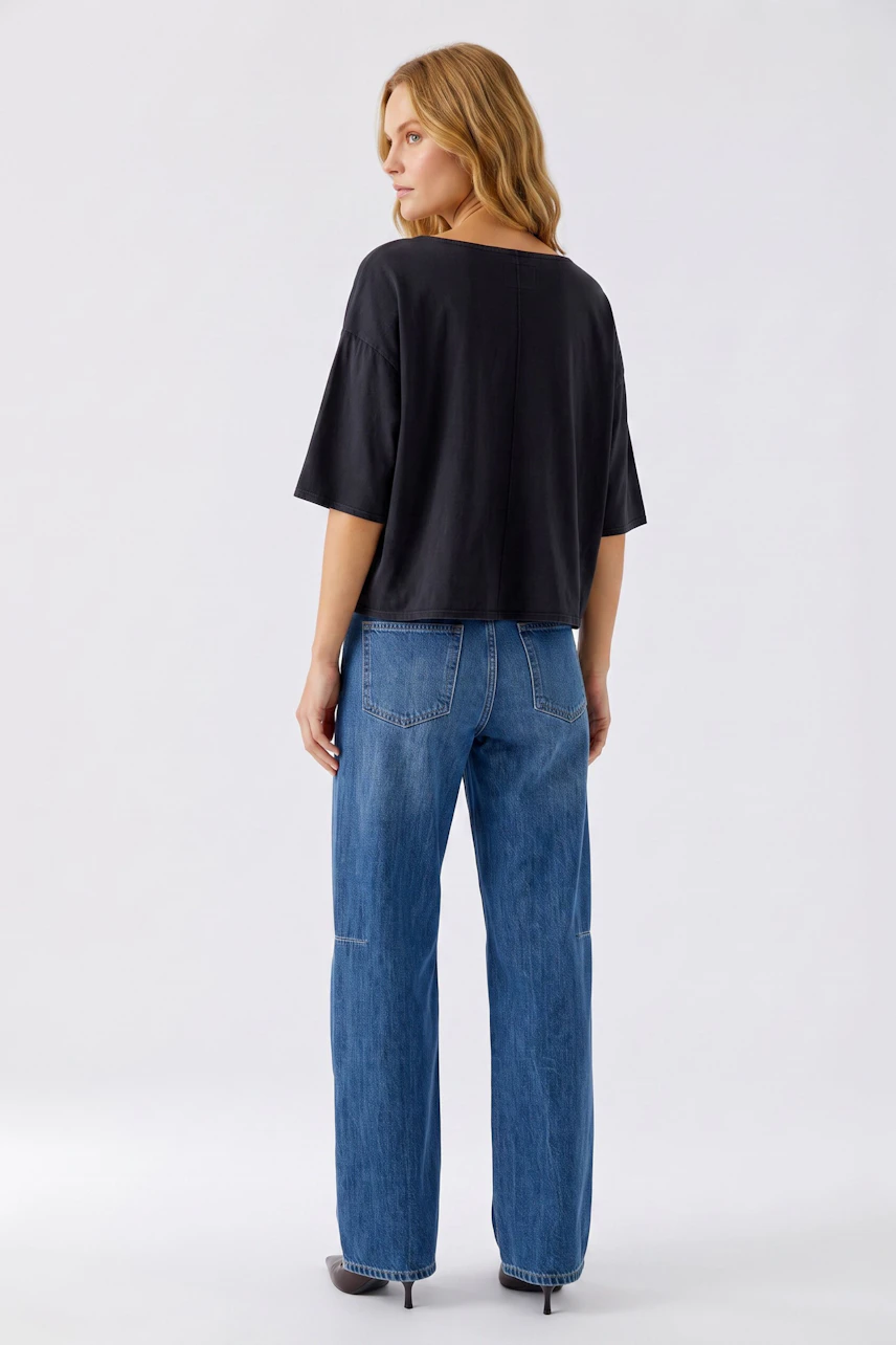 Casual women's T-shirt: Woman in a loose black T-shirt and blue jeans, standing confidently.