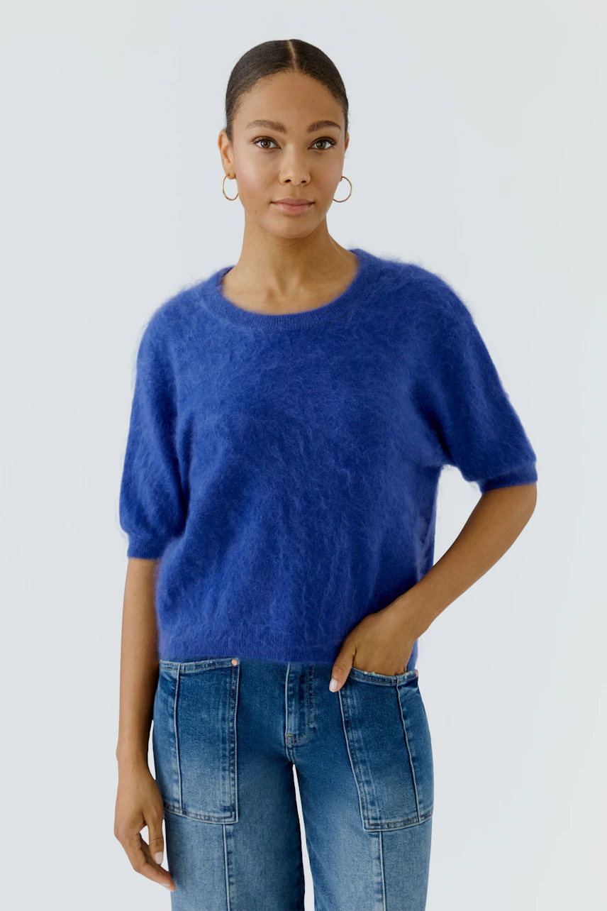 Frau im blauen Pullover mit kurzen Ärmeln und Jeans, lässiger Look.