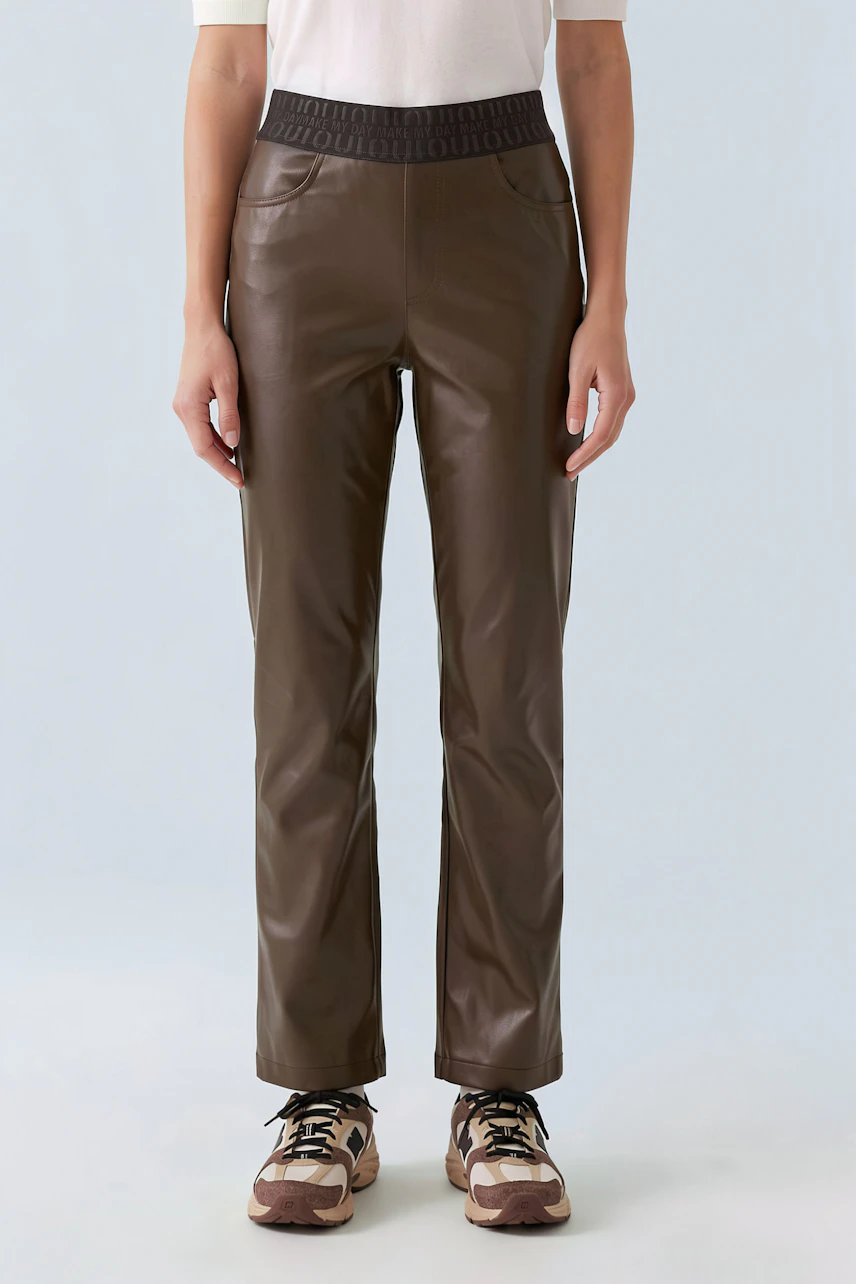 Woman in brown faux leather pants, white top, and sneakers. Casual and stylish look.