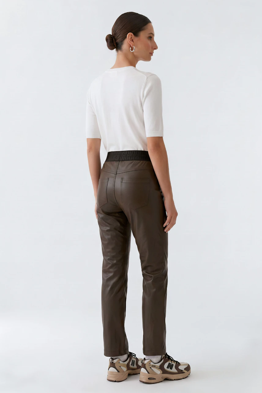 Woman in faux leather pants, white top, and sneakers, showcasing a casual, modern look.