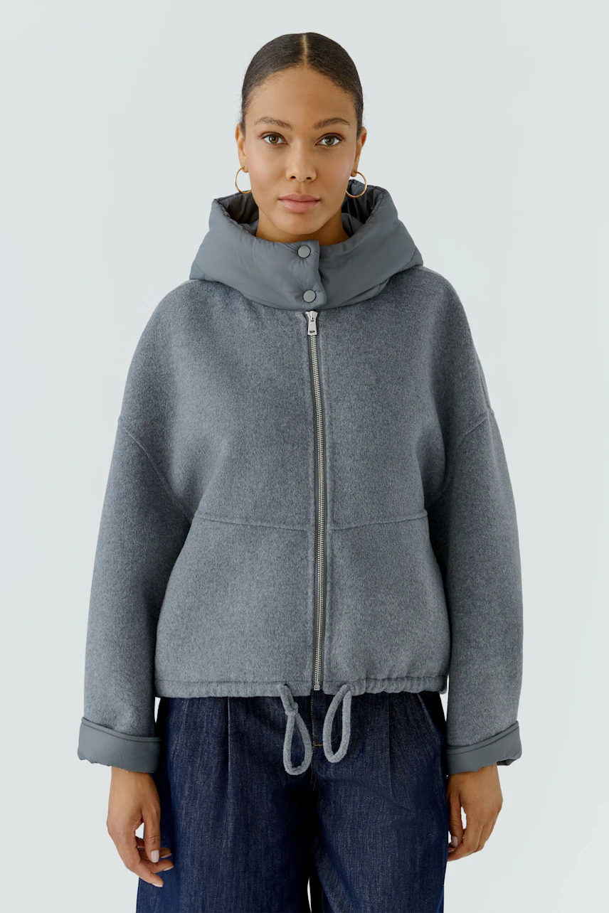 Casual women's jacket: Woman in a grey zip-up jacket with a hood, paired with dark jeans.