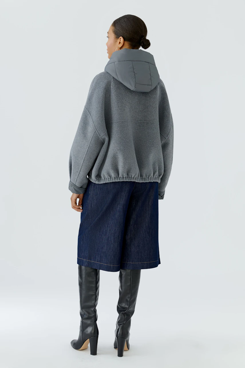 Casual women's jacket: Woman in a gray hooded jacket, denim culottes, and knee-high boots, facing away.
