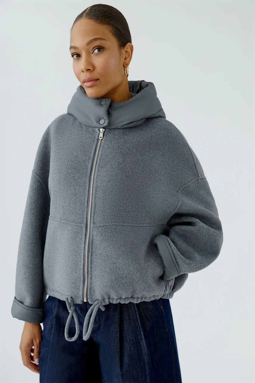 Casual women's jacket: Woman in a grey zip-up jacket with drawstring hem, paired with dark jeans.