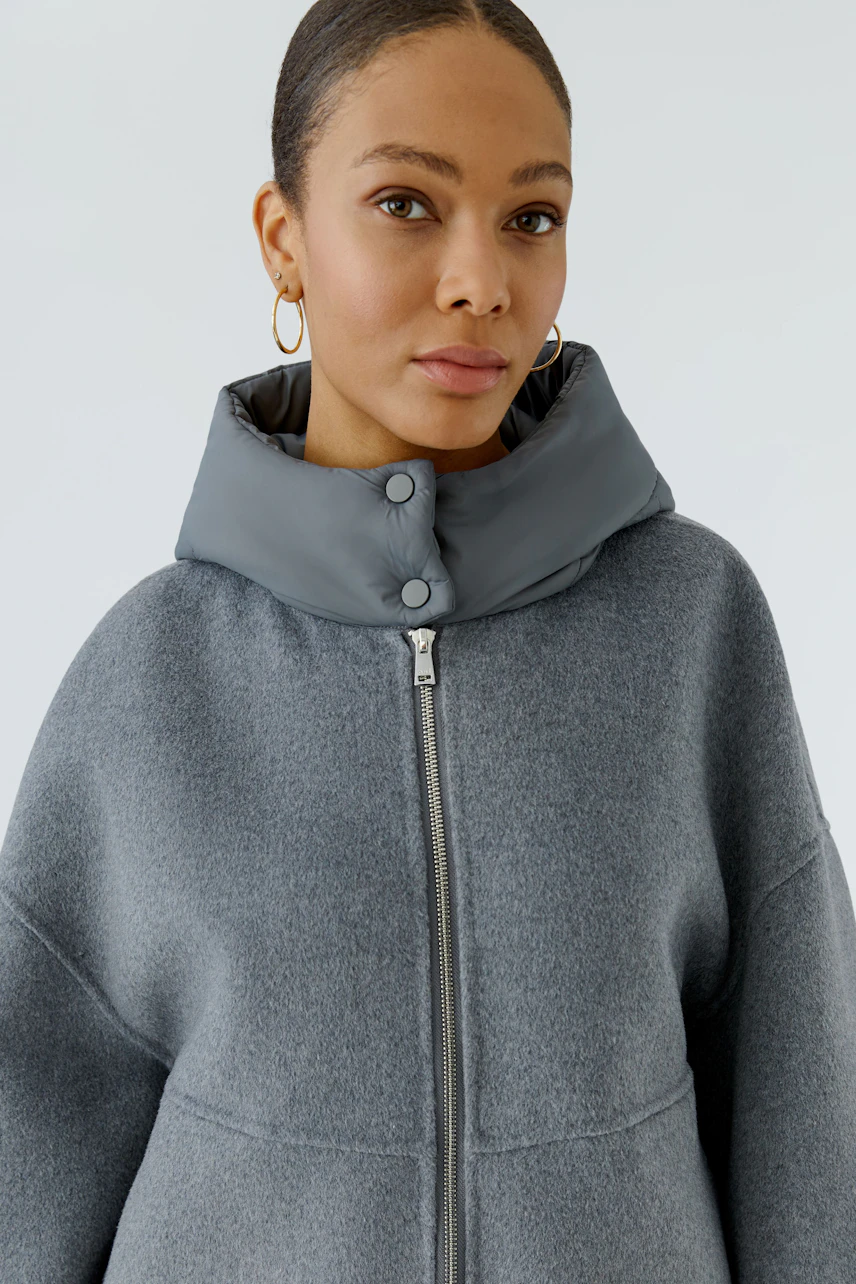 Woman in a grey jacket with a high collar and zipper, looking confidently at the camera.
