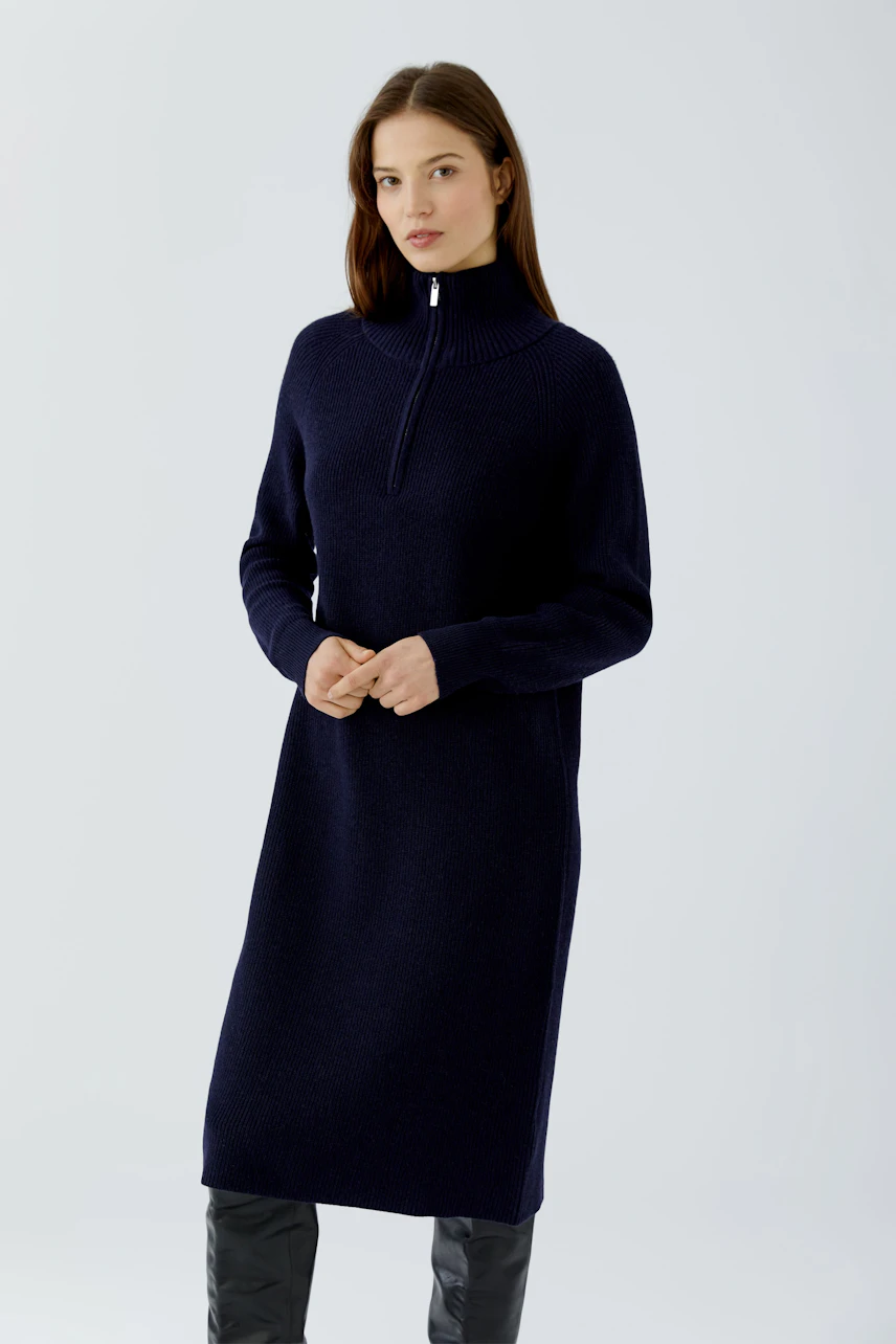 Knit dress: Woman in a navy knit dress with a high collar and long sleeves, paired with black boots.