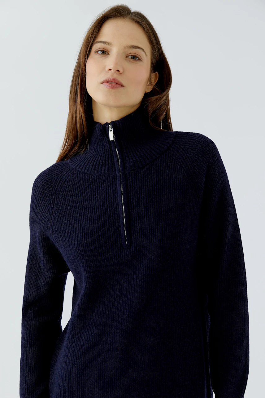 Woman in navy knit dress with high collar and zipper, exuding a casual and confident style.