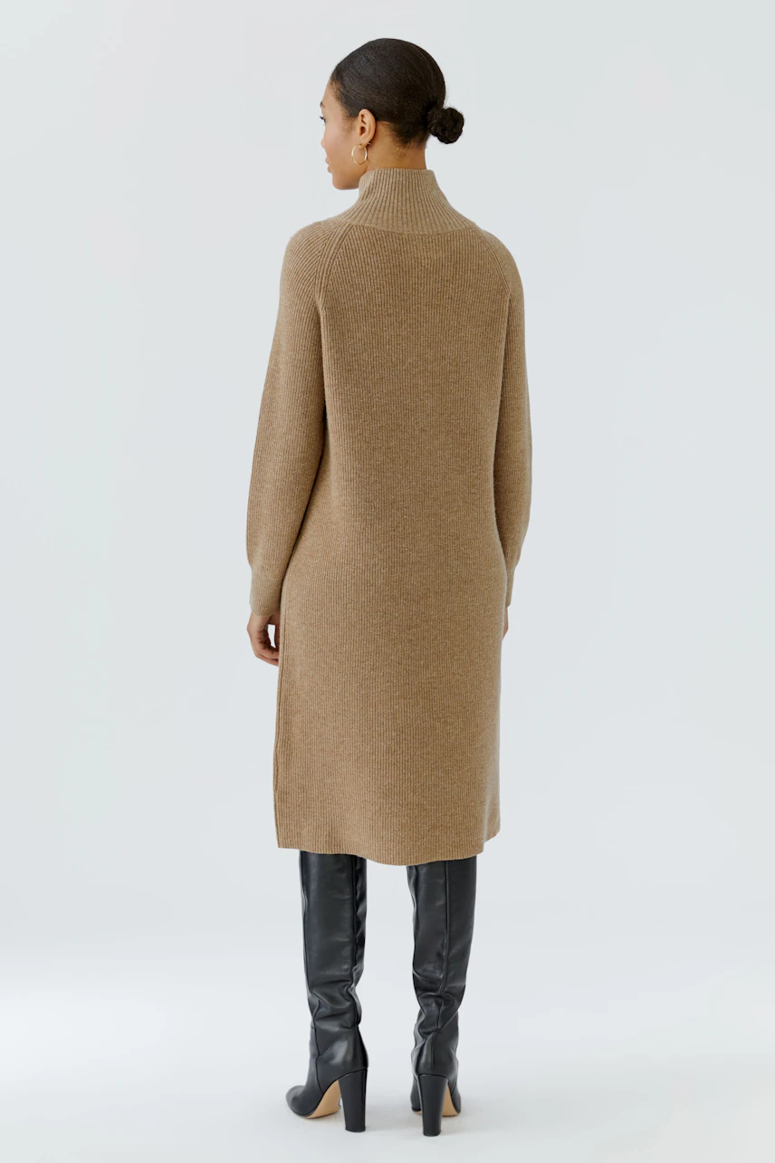 Woman in a brown knit dress, standing with back view, wearing tall black boots.