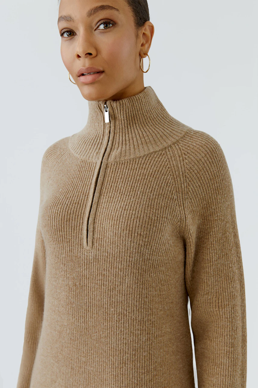Casual knit dress: Woman in beige ribbed knit dress with high collar and zipper, looking confidently.