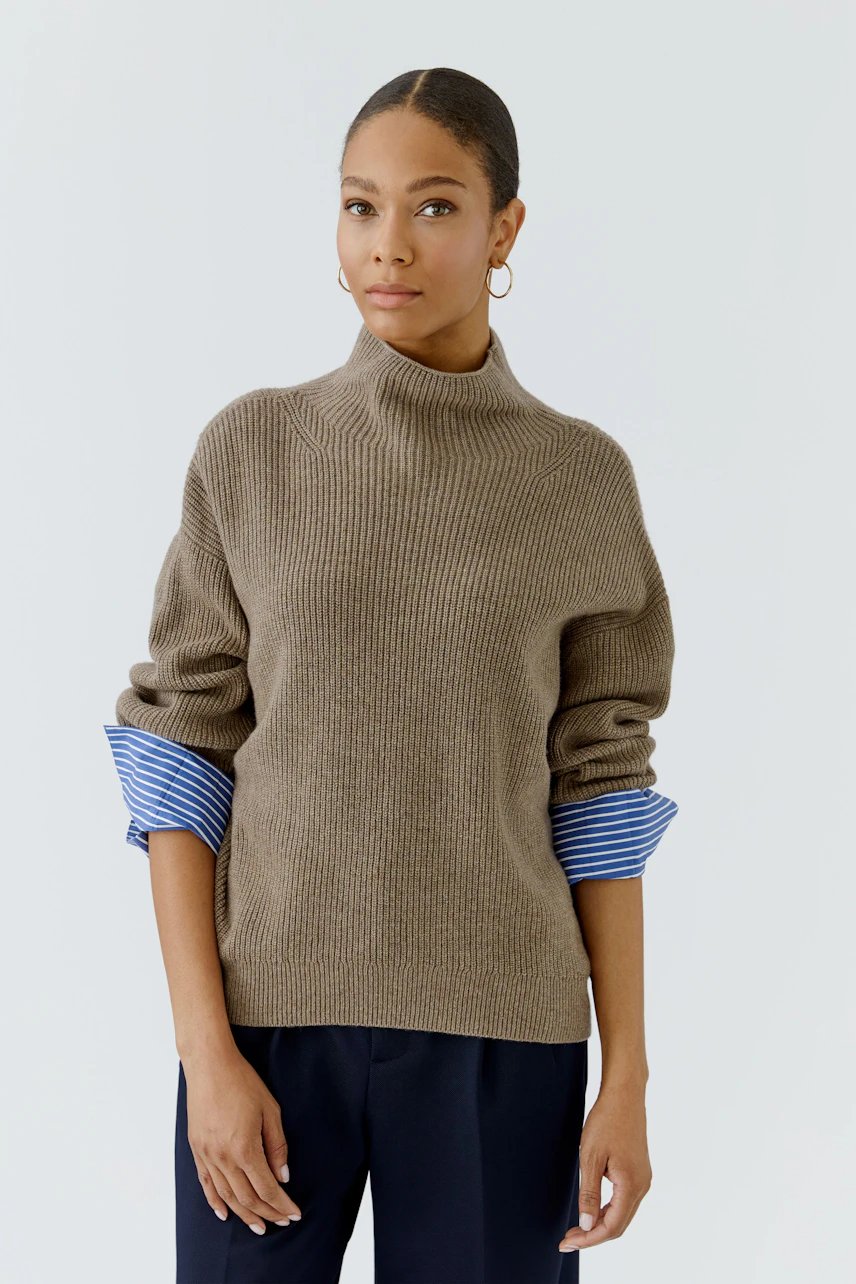 Casual women's pullover: Woman in a brown ribbed pullover with blue striped cuffs, looking poised.