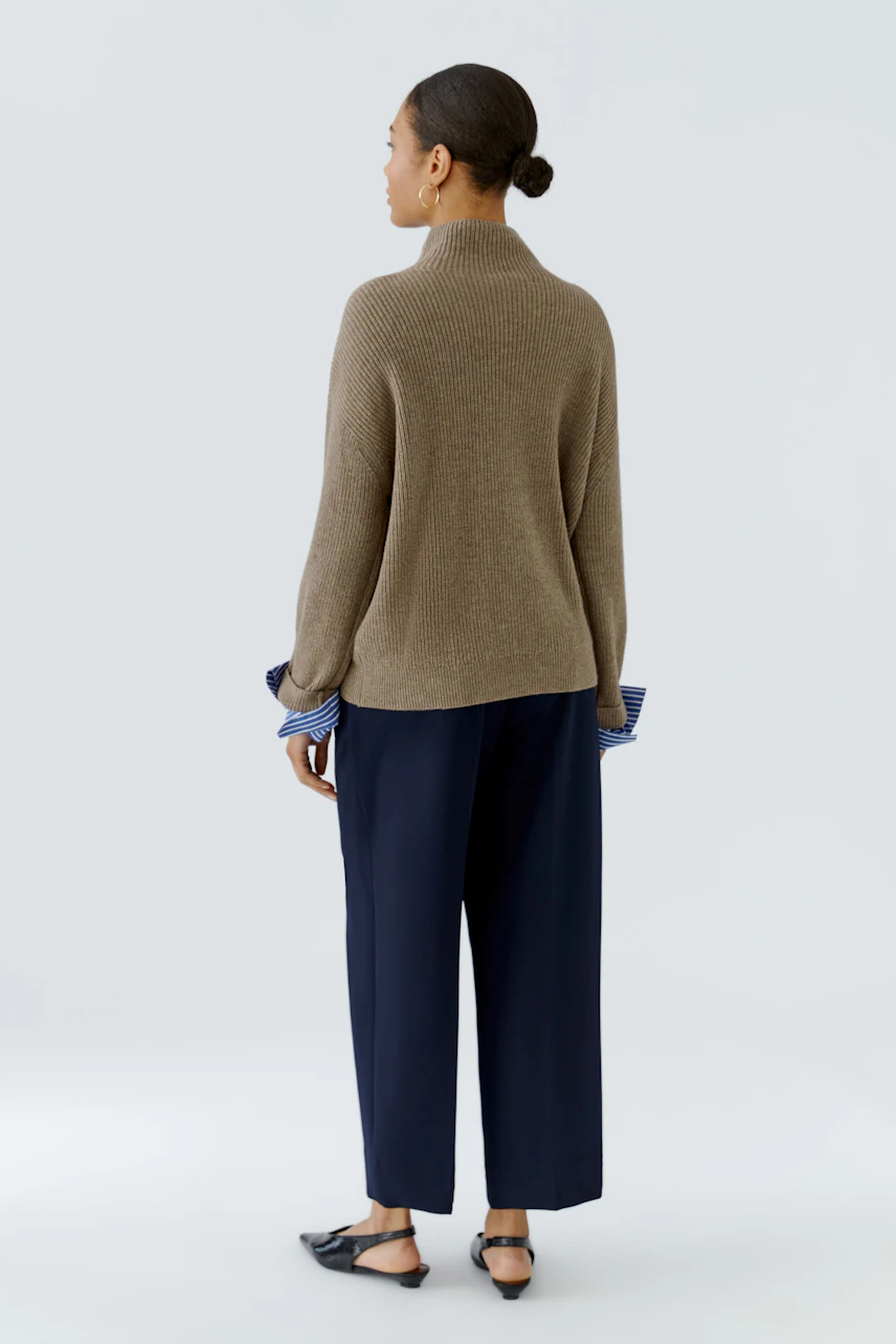 Casual pullover: Woman in a brown knit pullover with blue striped cuffs, paired with navy trousers.