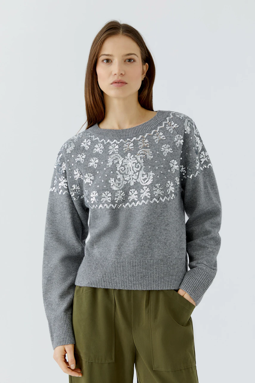 Casual women's pullover: Woman in a grey pullover with white floral patterns, paired with green pants.