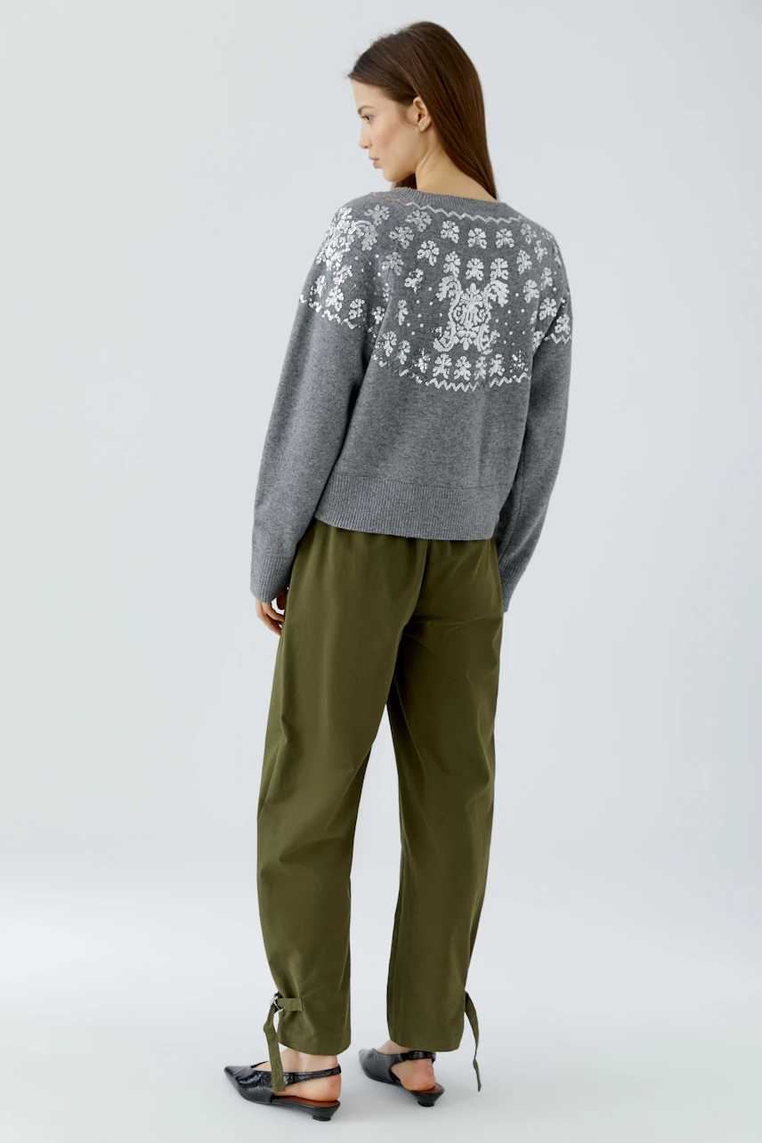 Casual women's pullover: Woman in a gray pullover with white patterns, paired with olive pants, looks relaxed.