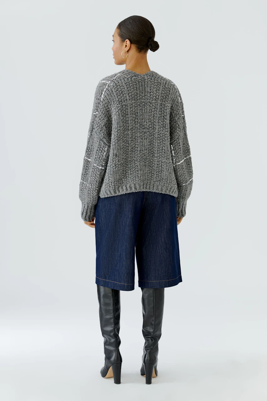 Casual knit cardigan: Woman in a gray cardigan, denim culottes, and knee-high boots, viewed from the back.