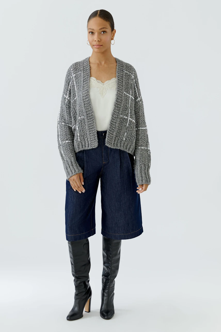 Casual cardigan: Woman in a grey knit cardigan with a white top and denim culottes, wearing black boots.