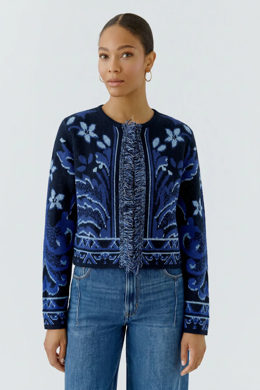 Strickjacke: Frau in blauer gemusterter Strickjacke und Jeans, schaut selbstbewusst.