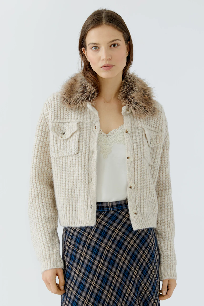 Woman in a cozy cardigan with faux fur collar, white top, and plaid skirt. Casual and stylish look.