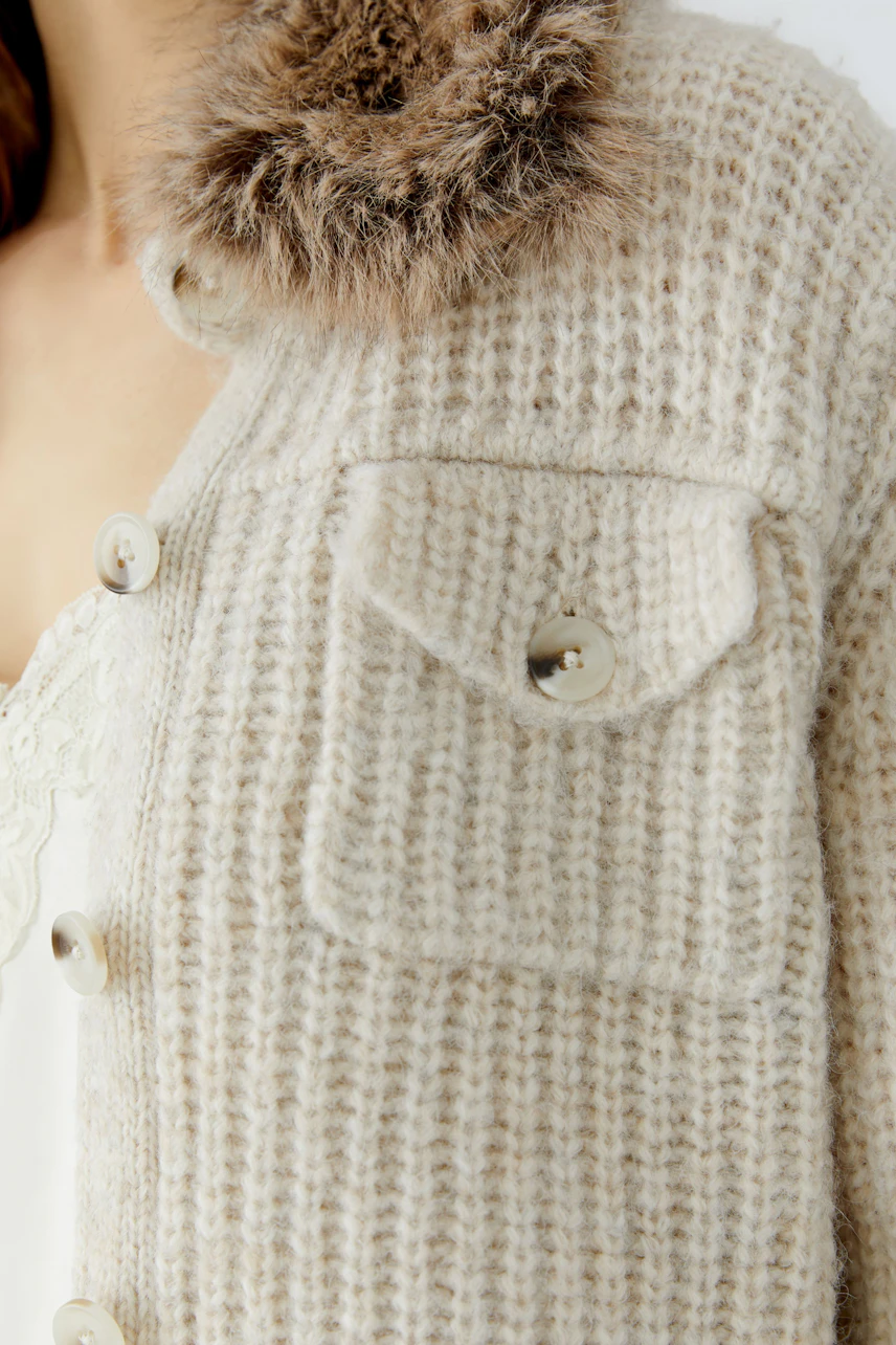 Woman in cozy cardigan with fur collar and button details, showcasing texture and style.