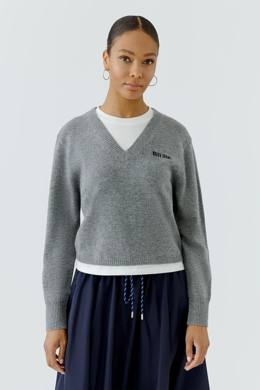 Casual women's pullover: Woman in a grey V-neck pullover over a white shirt, paired with a navy skirt.