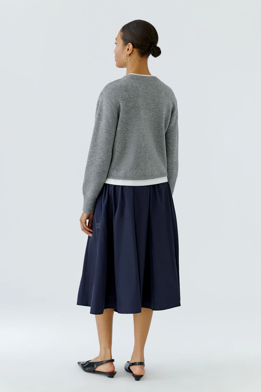 Woman in a gray pullover and navy skirt, standing with a relaxed posture, showcasing casual style.