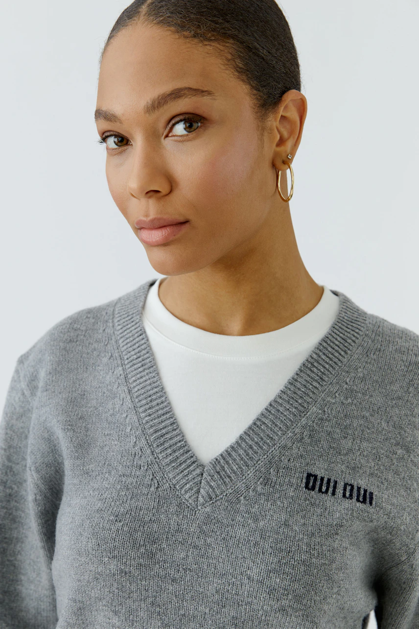 Casual women's pullover: Woman in a grey V-neck pullover with "Oui Oui" logo, layered over a white top.