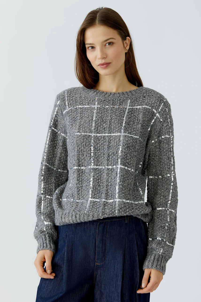 Casual women's pullover: Woman in a grey knit pullover with white grid pattern, paired with dark jeans.