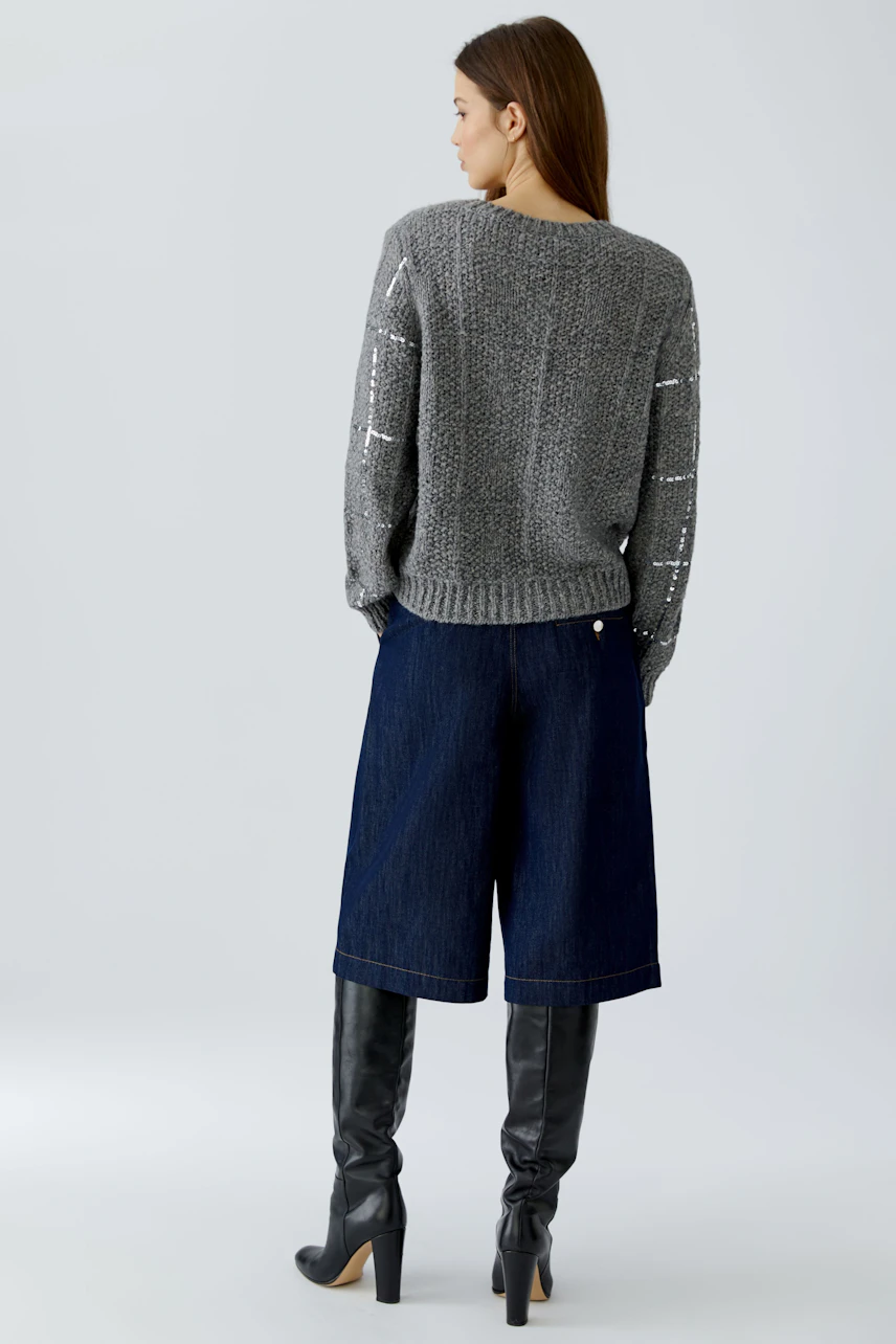 Casual women's pullover: Woman in a gray knit pullover, denim culottes, and knee-high boots, facing away.