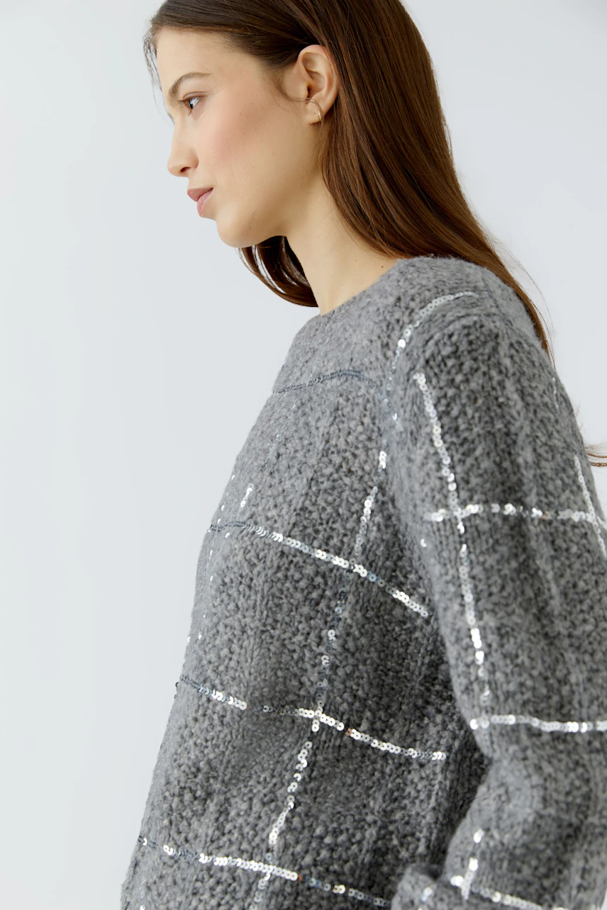 Woman in a textured grey pullover with shiny accents, looking to the side.