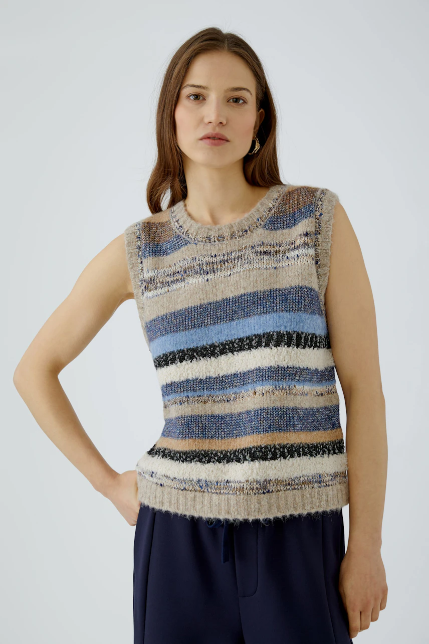 Casual women's pullover: Woman in a striped sleeveless pullover with blue and beige tones, looking relaxed.