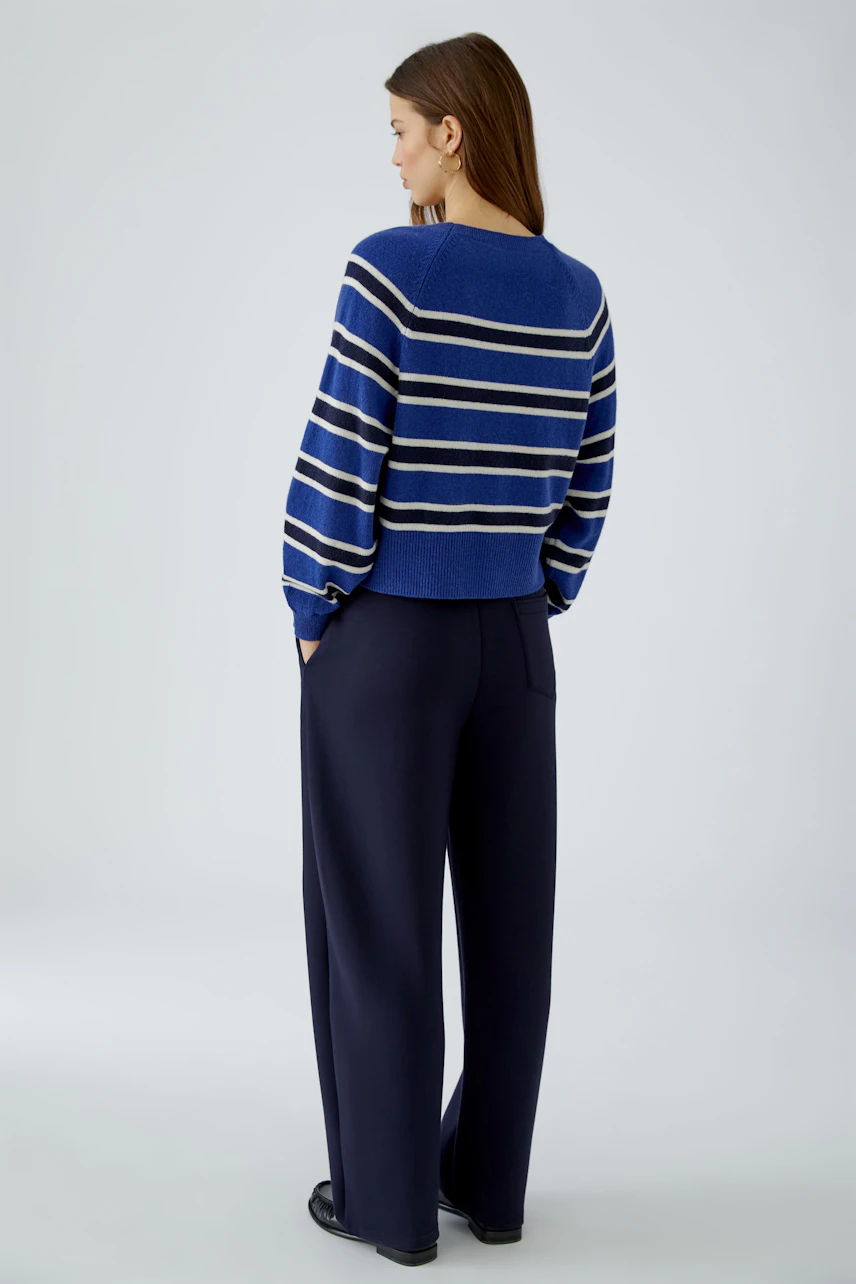 Casual women's pullover: Woman in a blue striped pullover and navy pants, viewed from the side.
