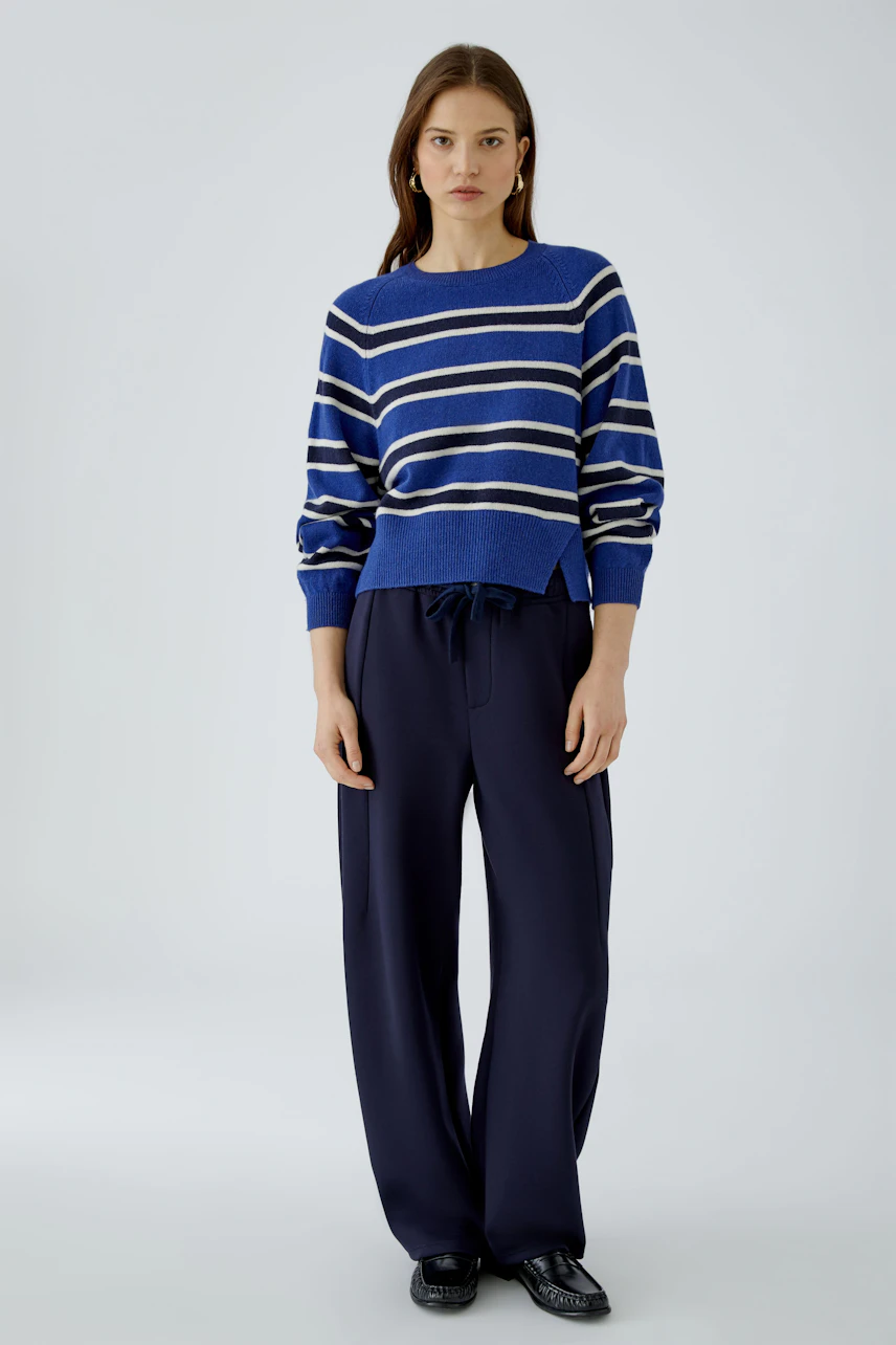 Casual women's pullover: Woman in a blue and white striped pullover with relaxed navy pants stands confidently.
